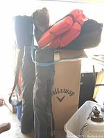 Several black carry bags containing folding chairs stacked upright alongside cardboard boxes and other items