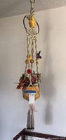Full view of the hanging planter showing the yellow ceramic bowl with faux plant and macrame knots with parrots attached.