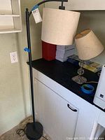 Floor lamp with black metal frame and beige fabric drum shade, two table lamps on black countertop with beige shades and assorted bases.