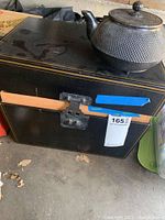 The Oriental style cast iron tea pot on top of a black box showing the shape and hinged lid with knob.