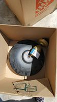 Top view of light fixture in box showing round black base with gold mounting bracket