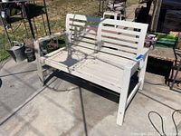 Wooden white painted patio bench viewed front-facing showing two seating sections and armrests, outdoor setting.