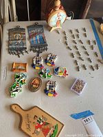 Overview of Romanian souvenir magnets and religious artifact items on table including painted wooden flask, metal wall hangings, resin magnets, and wooden plaques.