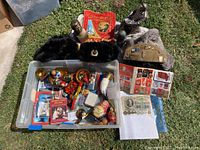 Overview of lot showing Communist banner, busts, metal sculptures, winter hats, pins, stamps, souvenirs and nesting dolls in plastic bin on grass