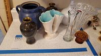 Wide view showing all vases on a countertop including ceramic, glass, and decorative items.