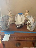 Full view showing teacup set, colonial figurines, and porcelain wall planters on a wooden surface.