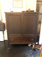 Front view of vintage wooden dresser with two doors and one drawer, showing dark stain and missing handles.
