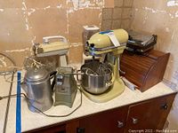 Overview of all kitchen appliances including mixer, waffle grill, can opener, percolator, blender, wooden bread box, and scale.