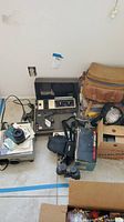 Overview of the lot showing multiple vintage photo and video equipment items on the floor including cameras, projector, leather bag, and light equipment.