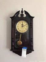 Full view of dark wood Westminster chime wall clock with pendulum visible.