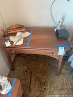 Wooden vanity table with some items on top, including a cordless phone and small desk accessories. Table is medium-brown wood with one drawer.