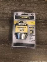 Front view of new Defiant deadbolt lock in unopened packaging showing branding and product details.