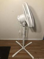 Side view of white pedestal fan showing blade housing, adjustable height stand, power cord, and four-legged base.