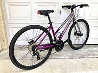Rear diagonal view of Schwinn Circuit hybrid bicycle showing rear disc brake, derailleur and purple and silver frame