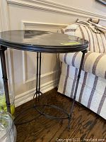 Side view of black metal accent table with round top next to a striped sofa on a wood floor