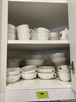 Photo showing multiple stacks of white ridged cups, bowls, and plates inside a cabinet.