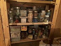 Shelf with various glass and plastic jars containing decorative beads, stones, shells, and small craft materials