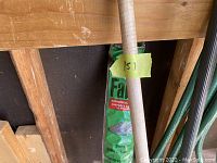 Close-up showing bag of grass seed labeled 'Fast' with a wooden handle of a tool in front