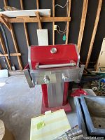 Closed view of KitchenAid red BBQ grill showing stainless steel burners and two control knobs with a thermometer on the hood.