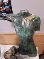 Frontal view of green-patina torso sculpture with cherub bust at base