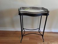 Side view of the black metal display cart showing curved legs and scalloped edge top with mirrored surface.