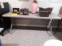 Full view of the plastic folding table with items displayed on top, showing size and condition.