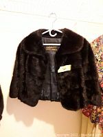Front view of the dark brown real fur jacket on a hanger, showing the collar and open front revealing interior lining with brand label.