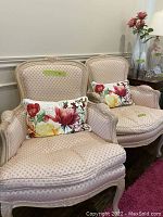 Pair of pink upholstered feather pattern accent chairs with carved wooden frames and two floral throw pillows