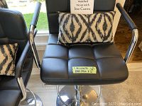 Front view of one adjustable black bar stool with chrome base, footrest, armrests, and patterned lumbar support pillow.