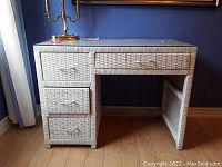 Front view of white wicker desk showing three vertical drawers on the left and two horizontal drawers along the front top.