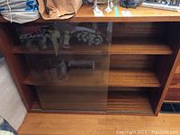 Front view of the solid wood bookcase showing the glass sliding door partially open revealing the two permanent shelves inside.