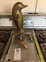 All three brass dolphin pieces displayed together on a stovetop showing size comparison and finish.