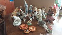 Photo showing a collection of small ceramic figures including animals (polar bear, mouse), children, and two small wooden bowls painted with traditional patterns, plus a wooden spinning top toy.