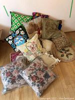 Full view of the stacked cushions showing various colors and patterns, mostly needlepoint and fabric cushions packed together.