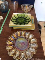 Various pieces including green glass egg dishes stacked in boxes, opalescent orange carnival glass egg dish, and a footed brass candy dish.