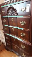 Front view showing dark wood dresser with brass drawer pulls and shell motif on top drawer. Green protective tape on drawer edges.