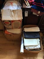 Three boxes filled with folded assorted fabric pieces including solid colored rolls and sheets.