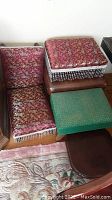 Top view of red floral fabric footstool and brown leather footstool with green fabric footstool and wooden footstool partially visible.