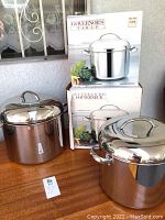 Two stainless steel stockpots on wood table next to their boxes, showcasing their polished finish and lids.