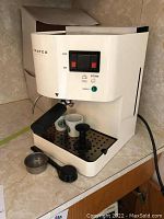 Full front view of the white Proteo Grande espresso machine with 2 Starbucks espresso cups on the drip tray and espresso accessories placed in front.