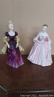 Two Royal Doulton porcelain figurines Loretta and A Hostess of Williamsburg displayed side by side, showing full front detail and scale for lot.