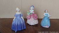 Front view of three Royal Doulton porcelain figurines in colorful period dresses, placed side by side.