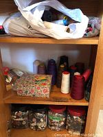 Shelf with multiple large cones of thread in various colors, a floral box, and plastic containers of buttons underneath