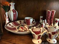 Grouped ceramic set showing large plate, cup and saucer, salt and pepper shakers, floral candle holders, and vases all decorated with Ukrainian red and white motifs.