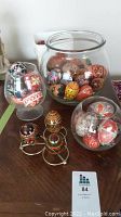 Clear glass bowl filled with various hand-painted Ukrainian decorative eggs in diverse colors and patterns, several wooden eggs on metal holders nearby.