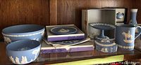 Wide shelf shot showing large and small bowls, stacked boxed plates, footed compote, lidded box, and mug with white relief decoration