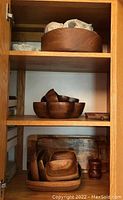 Three shelves inside cabinet showing multiple wooden bowls and serving trays stacked and nested.