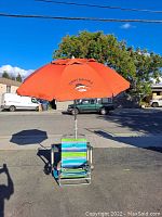 Photo showing one beach chair with attached tilted orange Tommy Bahama umbrella.
