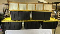 Five black stackable storage containers with yellow lids arranged in two rows, showing size and shape clearly.