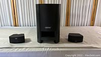 Front view of Bose subwoofer with two satellite speakers on each side, showing size and design